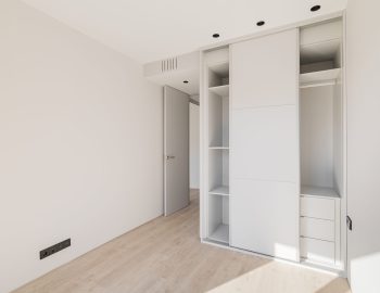 Empty clean bright bedroom with light wooden parquet and white wardrobe with sliding doors. A wardrobe is a useful and functional piece of furniture that saves space perfectly